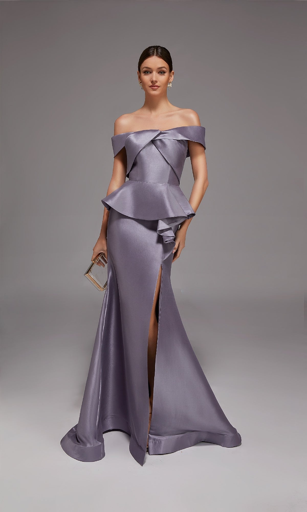 A woman poses against a plain gray background in the Alyce 27827 long formal dress—an off-shoulder, metallic lavender gown with a peplum waist and high slit—holding a small clutch.